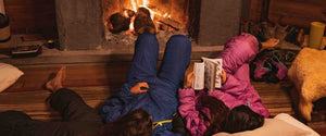 Two adults wearing their Selk’bag 6G Lite sleeping bag with legs, relaxing indoors by a fireplace